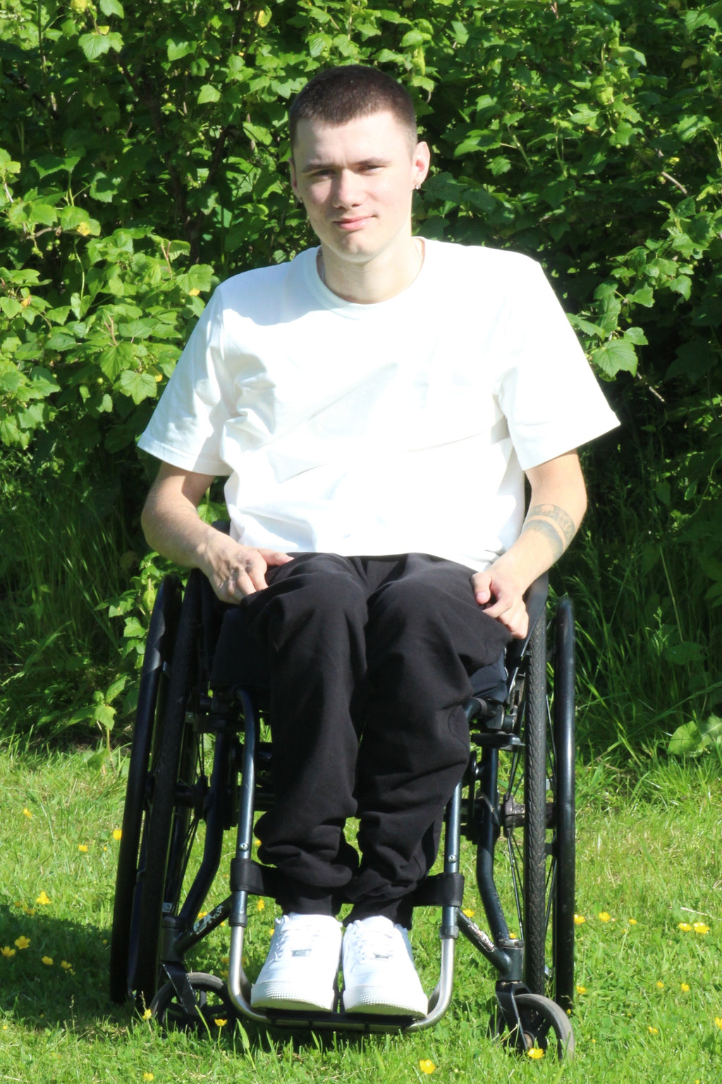 Young man using a manual wheelchair outdoors, wearing Vilber's adaptive joggers in black. Front view showing the elasticated waistband and relaxed fit through the seat.
