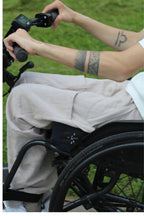 Close-up of a wheelchair user's hands on a Batec power add-on handlebar, with Vilber's beige summer trousers visible across the lap.