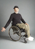 A man sitting in a wheelchair wearing Vilber's black long sleeve shirt and wheelchair adaptive trousers