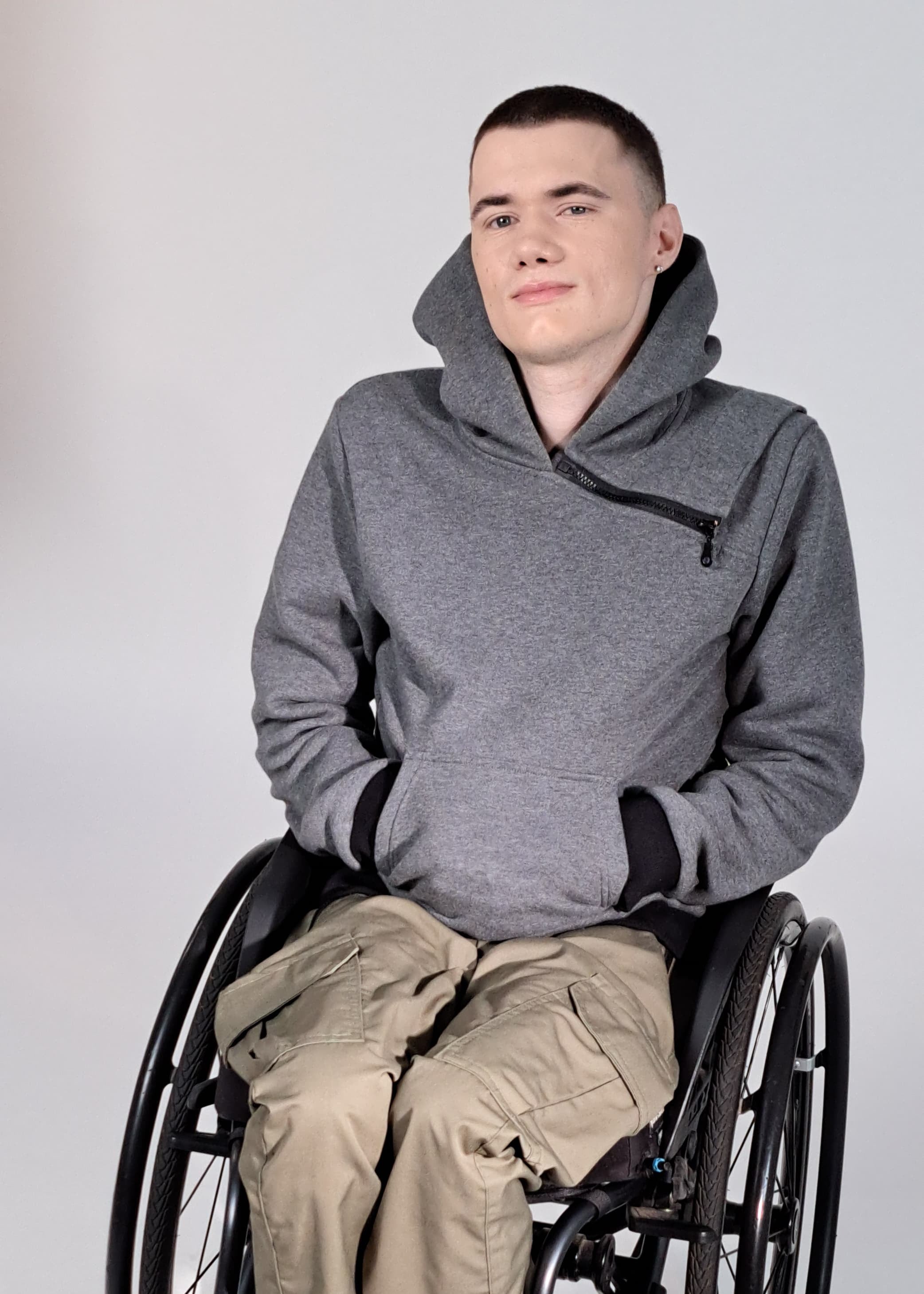 A young man sitting in a wheelchair and wearing grey melange adaptive hoodie designed for assisted dressing